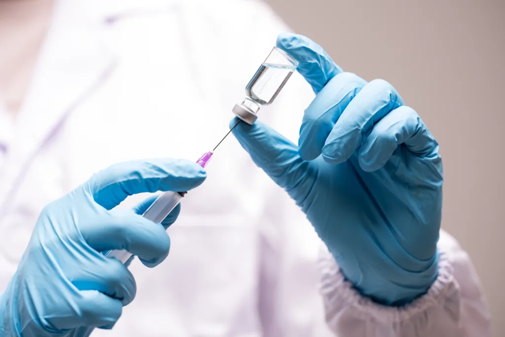 An image of a medical professional in blue gloves inserting a needle into a medicine vial